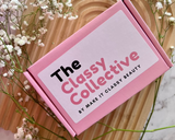 Pink packaging with 'The Classy Collective' branding surrounded by white flowers on a wooden and marble background.