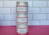 Stack of body butter containers with labels on a pink surface and tiled wall background