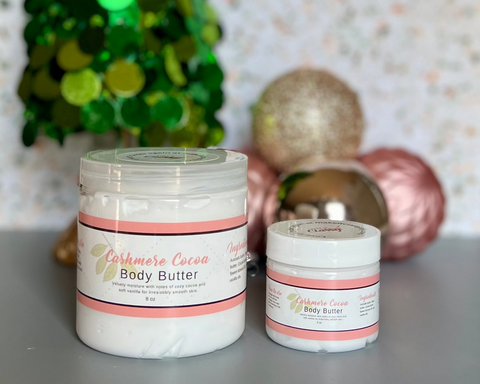 Two containers of body butter with a festive background featuring a green and gold tree.