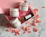 Set of skincare products in a decorative box with pink petals on a marble surface