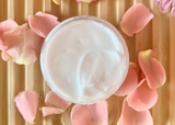Jar of cream surrounded by pink flower petals on a wooden surface