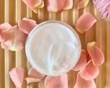 Jar of cream surrounded by pink flower petals on a wooden surface