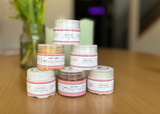 Stack of body butter containers on a wooden surface with a blurred background