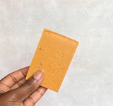 Hand holding a small rectangular piece of soap with a textured surface against a plain background