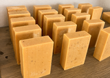 Handcrafted soap bars labeled 'Turmeric Orange Honey' on a wooden surface.